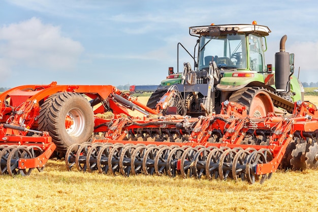 Foto ein leistungsfähiger landwirtschaftlicher traktor kombiniert mit einer roten mehrreihenförmigen scheibenharde an einem sommertag