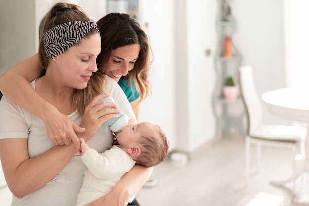 Ein lesbisches Paar, das ihrem Baby eine Flasche Milch schenkt, homosexuelle Eltern und Adoptionskonzept