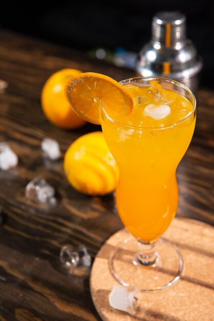 Ein leuchtend orangefarbener Cocktail mit Orangenscheiben und Eis in einer großen transparenten Glasplatte