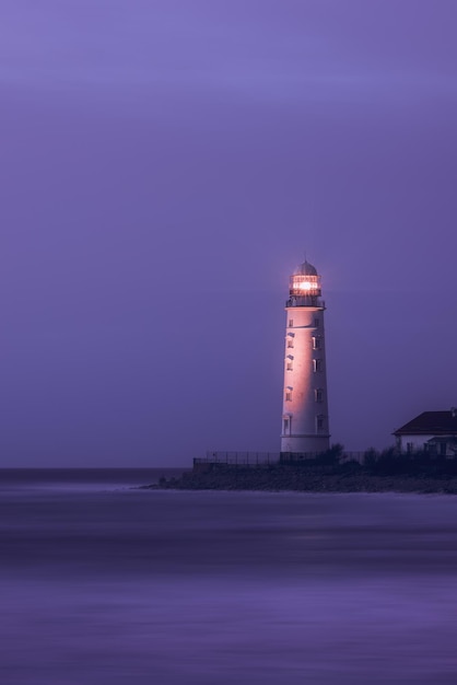 Ein Leuchtturm an der Küste des Meeres in der Abenddämmerung ist seine helle Lampe ein Wahrzeichen für Schiffe Seascape