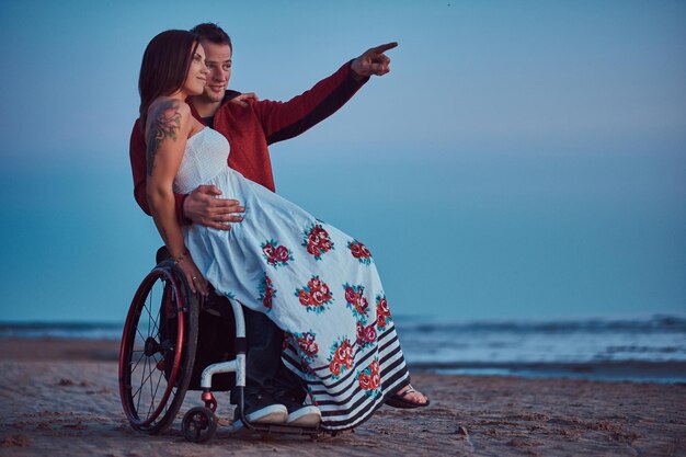 Ein Liebespaar, eine Frau sitzt auf dem Schoß ihres Mannes und ruht sich an einem Strand vor dem Hintergrund einer hellen Morgendämmerung aus.