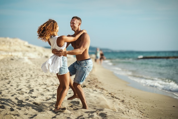 Ein Liebespaar hat Spaß, umarmt und spielt am leeren Sandstrand. Sie sehen sich an und lächeln glücklich.