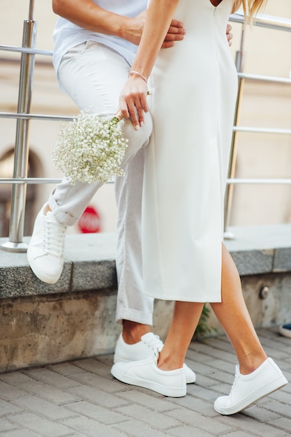 Ein Liebespaar in weißen Kleidern und Turnschuhen umarmt sich mit den Händen. Zukunfts- und Beziehungskonzept