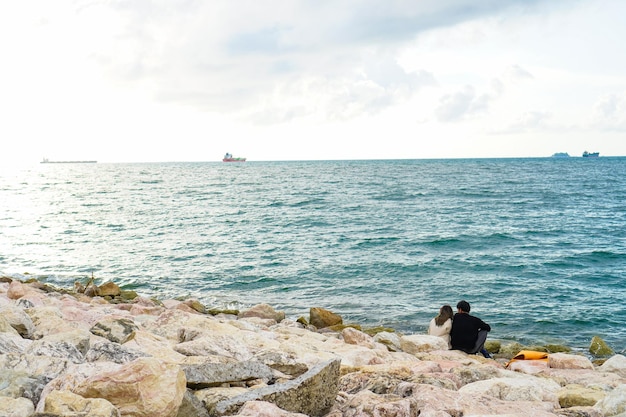 Ein Liebespaar sitzt am Strand mit dem Meer und den Frachtschiffen im Hintergrund