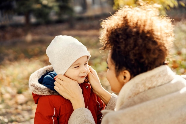 Ein liebevolles Kindermädchen passt einem kleinen Jungen bei kaltem Wetter eine Mütze zu, damit er sich nicht erkältet