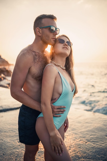 Ein liebevolles Paar geht am Strand entlang am Meer Junge Familie bei Sonnenuntergang am Mittelmeer Urlaubskonzept Eine Frau in einem Badeanzug und ein Mann in kurzen Hosen bei Sonnenuntergang am Meer Selektiver Fokus