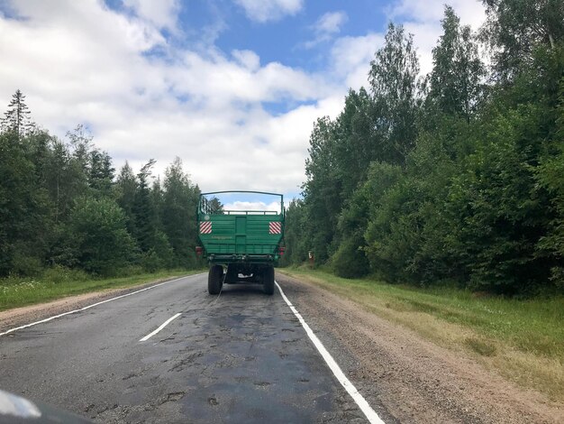 Ein LKW, ein Traktor mit einem großen grünen Anhänger, fährt auf einer Waldasphaltstraße