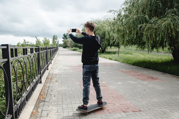 Ein lockiger Teenager europäischen Aussehens in einem schwarzen Hoodie, der auf einem Skateboard in einer Gasse steht...