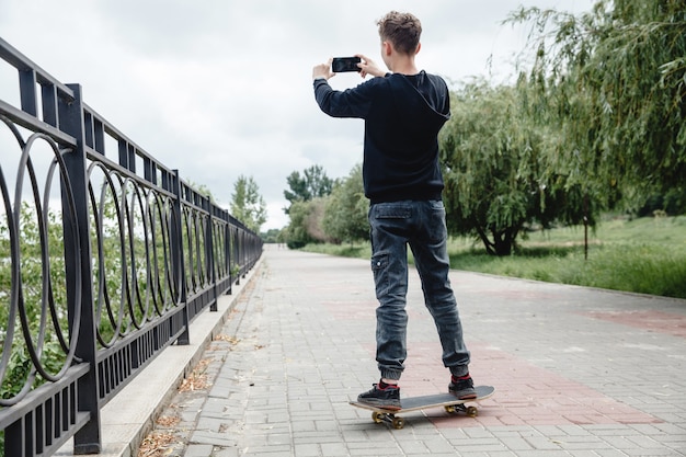 Ein lockiger Teenager europäischen Aussehens in einem schwarzen Hoodie, der auf einem Skateboard in einer Gasse steht...