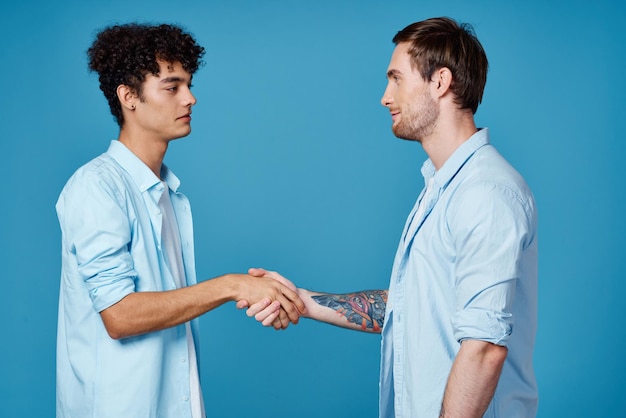 Foto ein lockiger typ in einem hemd steht neben einem jungen mann in einem t-shirt auf einem blauen hintergrund und hat eine hochqualitative fotoaufnahme.