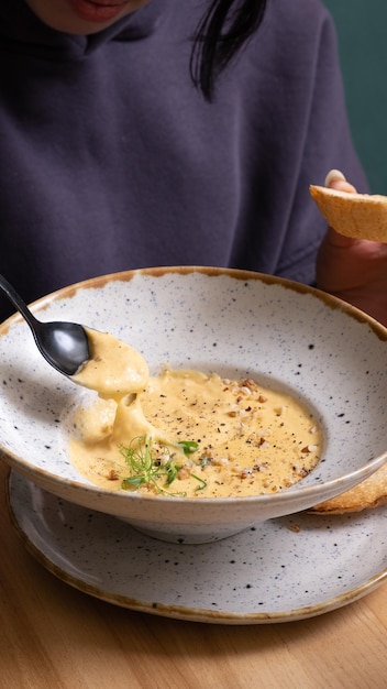 Ein Löffel in den Händen einer Frau mit einem Teller Käse-Creme-Suppe mit Nüssen und Grünen