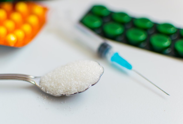 Ein Löffel Zucker eine Spritze und Pillen auf weißem Hintergrund Das Konzept der Schädigung von Zucker und das Auftreten von Diabetes