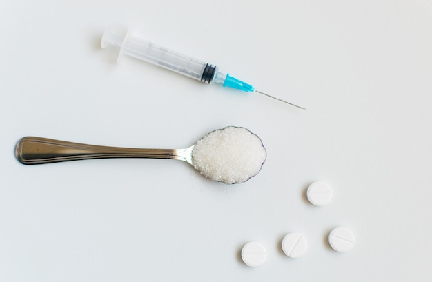 Ein Löffel Zucker, eine Spritze und Pillen auf weißem Hintergrund Das Konzept der Schädigung von Zucker und das Auftreten von Diabetes