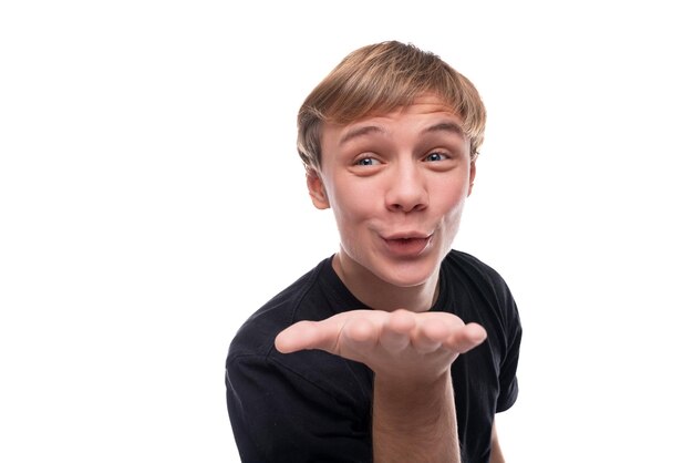 Foto ein lustiger blondhaariger teenager in einem schwarzen t-shirt schickt einen luftkuss