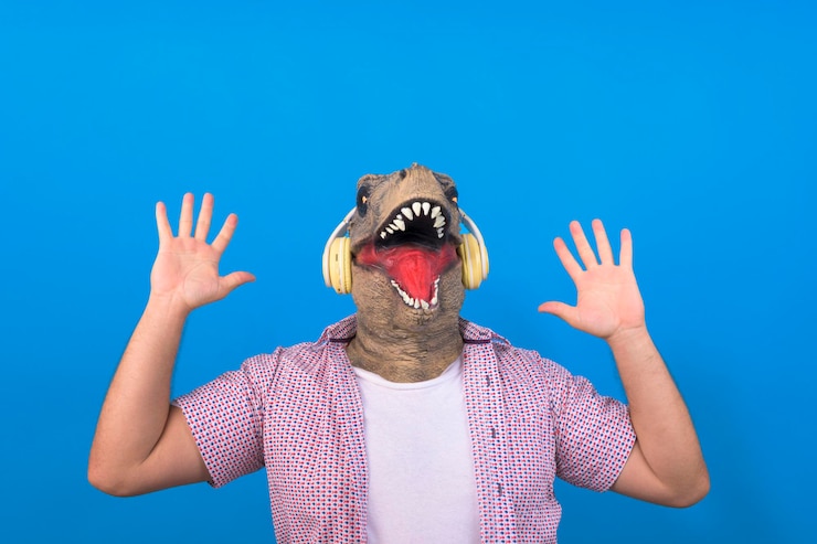 Foto ein lustiger kerl mit einem dinosaurierkopf, der fröhliche musik auf einem blauen, isolierten hintergrund hört