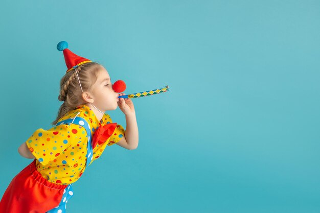 Ein lustiges Kind, ein Clown vor blauem Hintergrund, ein glückliches Kind, das mit festlichem Dekor spielt.