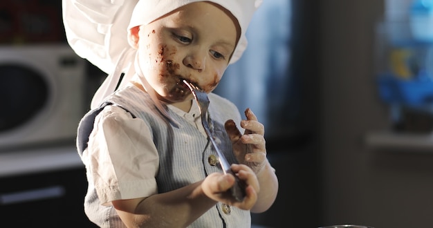 Ein lustiges Kind isst eine Schokolade mit der Gabel in der Küche