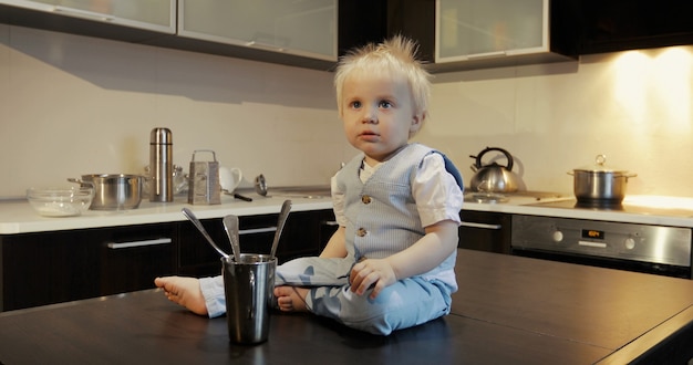 Ein lustiges Kind mit Gabel und Löffel in der Küche Porträt eines kleinen Jungen auf dem Tisch