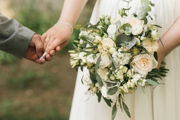 Ein luxuriöser Hochzeitsstrauß mit weißen Rosen in den Händen der Braut und des Bräutigams