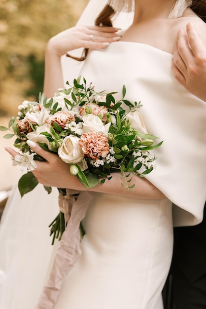Ein luxuriöser Hochzeitsstrauß mit weißen Rosen in den Händen der Braut