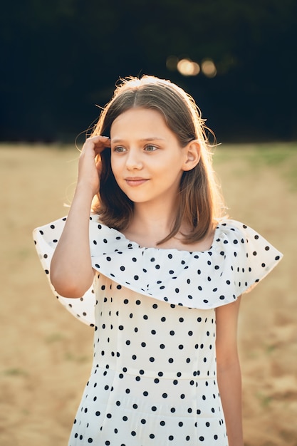 Ein Mädchen am Strand in einem gepunkteten Kleid schaut in die Ferne und glättet ihre Haare.