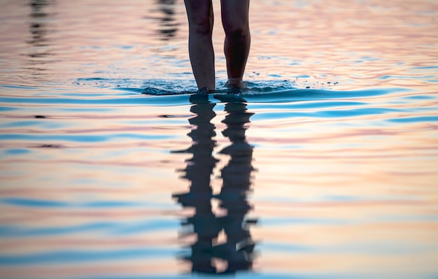 Ein Mädchen an der Küste bei Sonnenuntergang geht auf dem Wasser spazieren, nur die Beine sind sichtbar