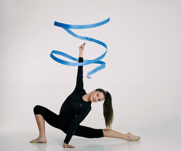 Foto ein mädchen aus der rhythmischen gymnastik in einem bodysuit dreht ein band, das auf einem halben schritt sitzt