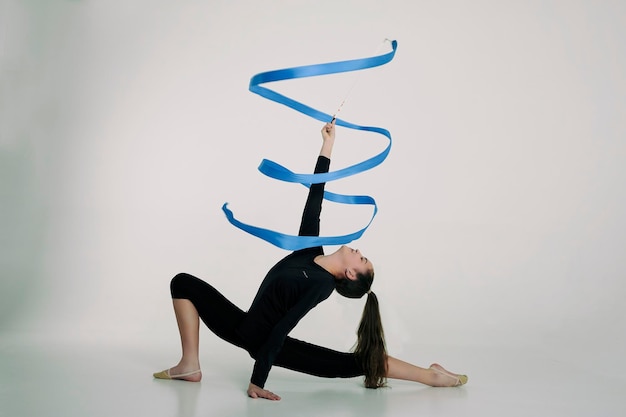 Foto ein mädchen aus der rhythmischen gymnastik in einem bodysuit dreht ein band, das auf einem halben schritt sitzt