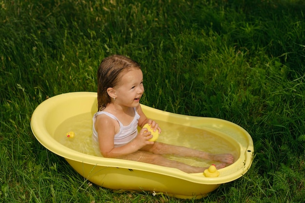 Ein Mädchen badet im Wasser in einer kleinen Wanne in der Natur im Freien und spielt mit Spielzeugenten