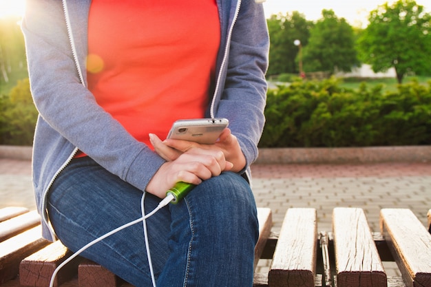 Ein Mädchen benutzt ein Smartphone im Freien, während es von einer externen Energiebank auflädt