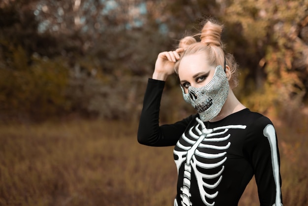 Ein Mädchen, das als Skelett verkleidet ist und eine Maske mit Strasssteinen trägt, sieht gruselig in die Kamera Halloween