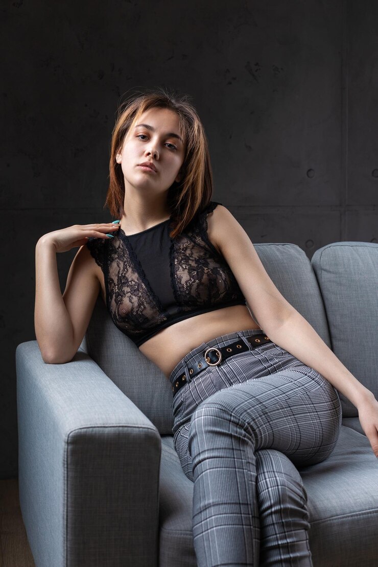 Foto ein mädchen, das in einem schwarzen spitzentopf gekleidet ist, posiert auf einem grauen sofa im studio