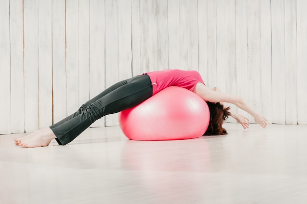 Ein Mädchen, das Lügenhaltung der Balance über einem rosa fitball in einer Turnhalle hält