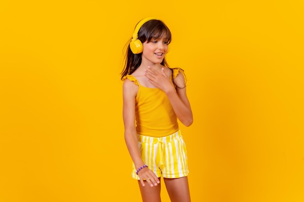 Ein Mädchen, das Musik hört und mit drahtlosen Kopfhörern tanzt, gelber Hintergrund