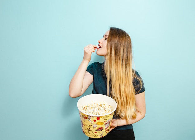Ein Mädchen, das Popcorn auf einem blauen Hintergrund isst.