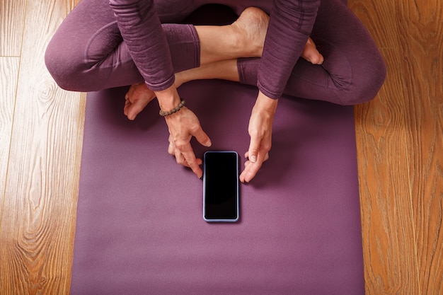 Ein Mädchen, das zu Hause Yoga und Meditation auf einem lila Teppich mit einem Smartphone und einer mobilen App praktiziert