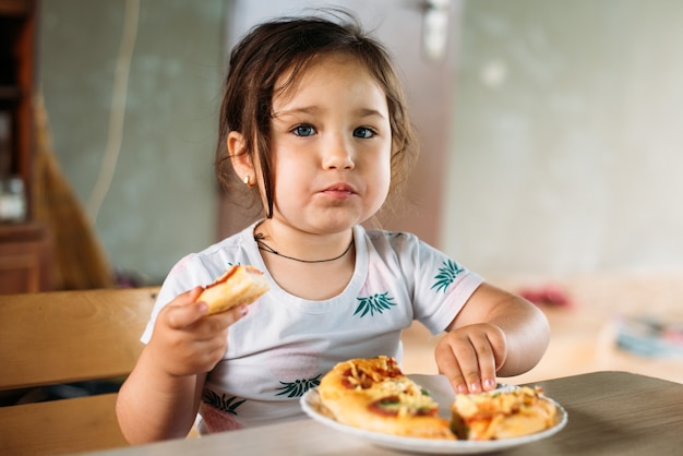 Ein Mädchen ein Kind auf der Straße isst eine Minipizza sehr appetitlich