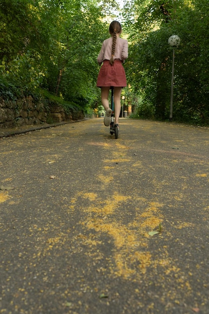 Ein Mädchen fährt auf einem Roller eine Gasse im Park entlang. Ein Kind fährt auf einem Roller im Park