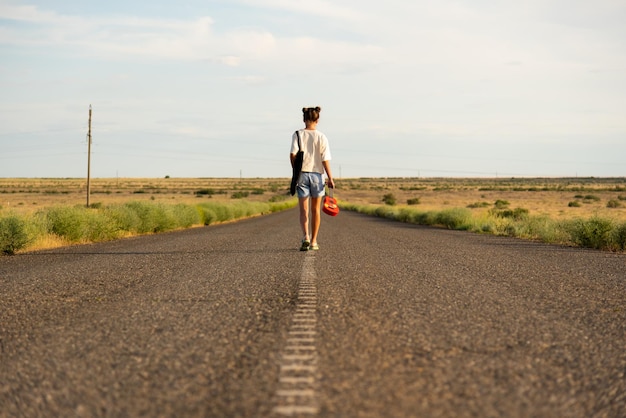 Ein Mädchen geht auf einer leeren Straße in der Steppe Sie hat eine Ukulele in ihren Händen Offene Straße