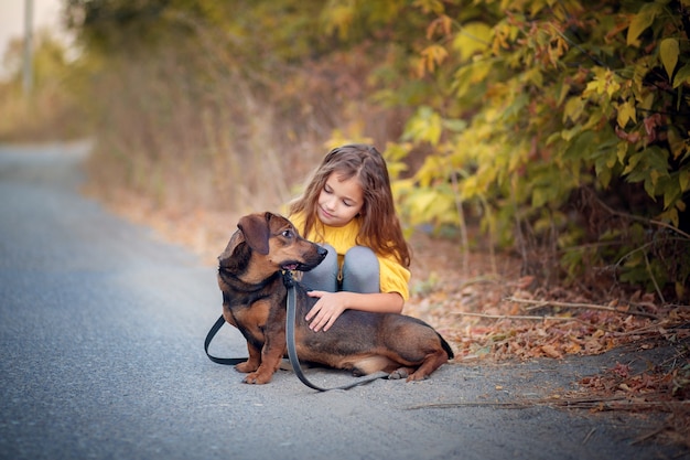 Ein Mädchen geht durch einen Herbst, der mit einem Dackelhund ausgepeitscht wird.