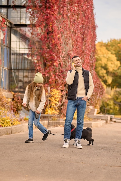 Ein Mädchen geht mit einem Hund spazieren, ihr Vater telefoniert