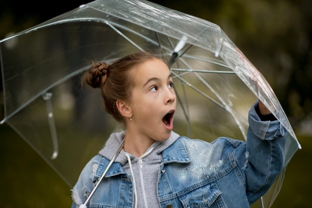 Ein Mädchen geht und spielt mit einem durchsichtigen Regenschirm im Park.