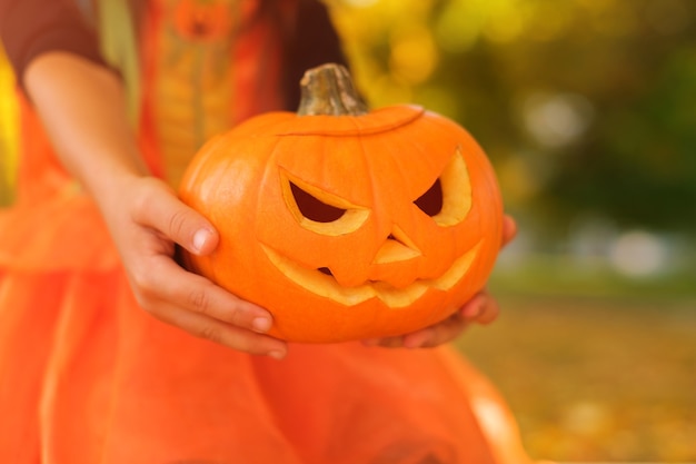 Ein Mädchen hält am Vorabend von Halloween einen Kürbis mit einem geschnitzten gruseligen Gesicht hin