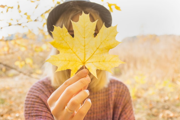 Ein Mädchen hält ein Ahornblatt in der Hand. Warmer Herbsttag, gelbe Herbstblätter. Herbstkonzept.
