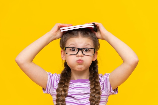 Ein Mädchen hält ein Buch und bläst ihre Wangen auf Ein süßes kleines Mädchen auf gelbem, isoliertem Hintergrund