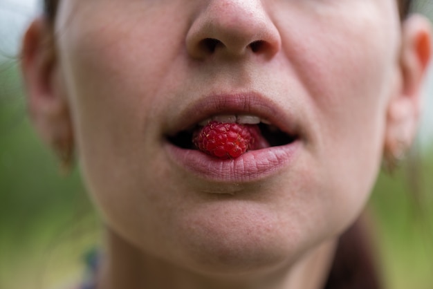 Ein Mädchen hält eine Himbeerbeere im Mund