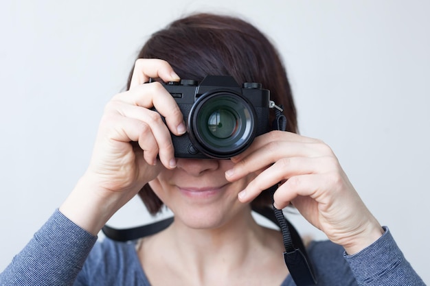 Ein Mädchen hält eine Kamera an ihrem Gesicht Das Objektiv sieht aus wie ein großes Auge Hobby mit Fotografie