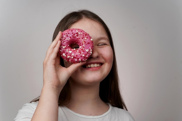 Ein Mädchen hält einen rosa Donut hinter ihrem Auge und lächelt.