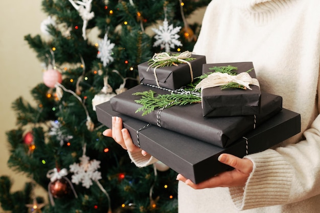 Ein Mädchen hält einen Stapel Geschenkkisten in den Händen und schließt einen geschmückten Weihnachtsbaum im Hintergrund an