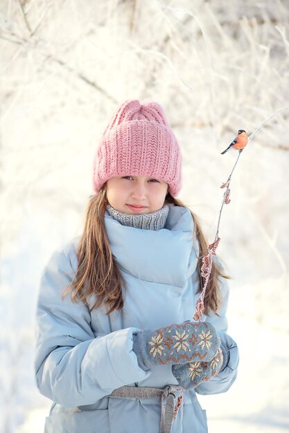 Ein Mädchen im Grundschulalter in einer rosafarbenen Strickmütze und einer blauen Jacke in einem verschneiten Winterwald